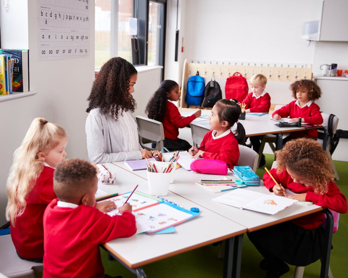 Children in red school uniforms sitting at desks in a classroom with a teacher.